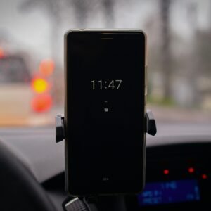 A smartphone mounted in a car with its screen showing the time in a blurred traffic environment.
