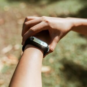 Crop unrecognizable female checking notifications on hand fitness tracker while exercising on green lawn on sunny summer day