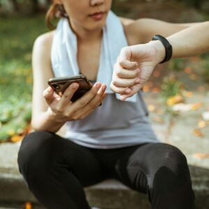 Anonymous female in sportswear using smartphone and smart watch after exercising on sports ground