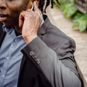 Crop well dressed black busy male having phone conversation and listening to interlocutor through wireless earbuds on street on summer day