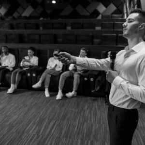 Monochromatic image of a speaker presenting to a small audience in a stylish auditorium.